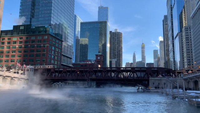 Steam rising from the Chicago River as temperatures plunge and an elevated 'el' train crosses a bridge.