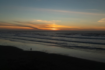 Fototapeta na wymiar Man walking on the beach at sunset on the Oregon coast