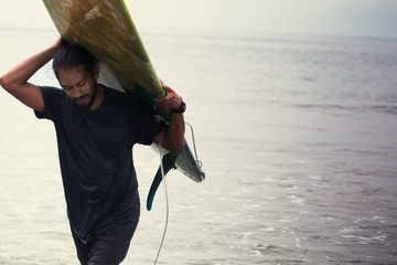 Mixed race male surfer carrying  long board from ocean