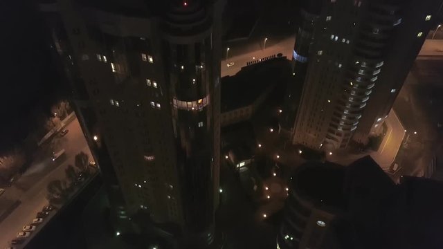 drone is flying down along high residential complex in night time, lights in windows