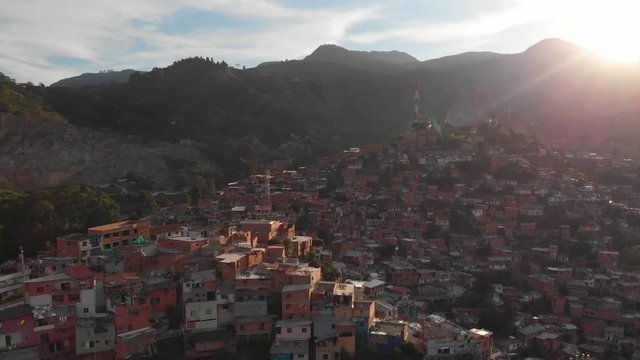 Flying over poor hillside slum in Colombia Comuna 13 aerial shot with sunset in background