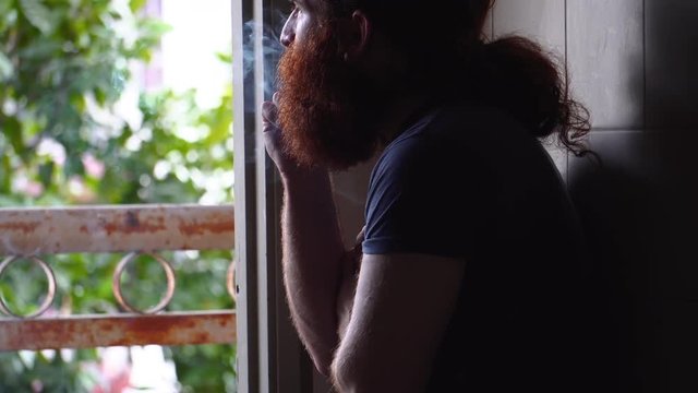 Bearded man semi close up smoking indoors what appears to be a marijuana cigarette