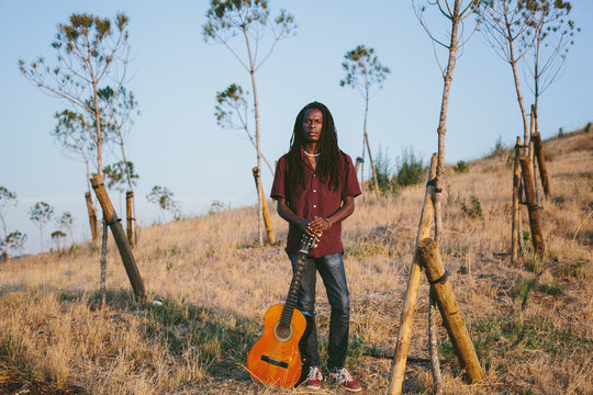Portrait of musician African man  wearing dreadlocks holding guitar outdoor