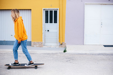 Street portrait of positive young female wearing orange hoody riding with skateboard in city
