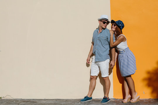 Happy smiling couple near orange sunny wall outdoor. Summer vacation, enjoy holiday