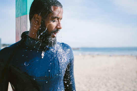 Portrait of african surfer man taking a shower on the beach. Mixed race, dark skin and beard. Summer sport activity