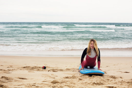 Happy funny positive female surfer with surf board on ocean beach doing exercises