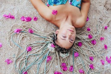 Young woman wearing braids hair style lying on sea shore with pink flowers in her hair