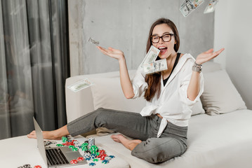 Stylish young brunette girl betting and playing poker online on laptop, winning money in internet...