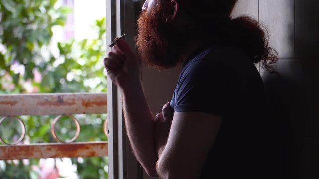 Bearded man smoking what appears to be a marijuana cigarette indoors alone in shadow area