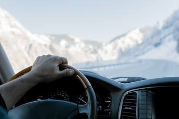 Close-up of a man's hand on the steering wheel of a car that moves on a snowy road among the mountains in the winter