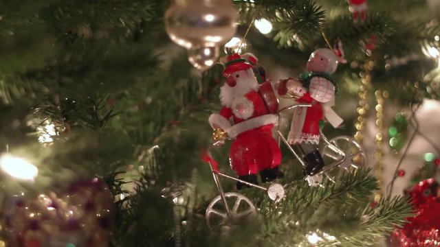 Mr. & Mrs. Claus riding a bike Christmas ornament that is hanging on a Christmas tree.