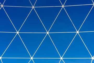 Metal white lattice in the form of geometric shapes on a background of blue sky