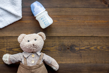 Feed baby concept. Teddy bear toy near small bottle with food on dark wooden background top view copy space