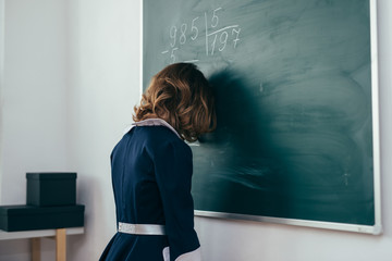 Schoolgirl stands with her forehead on the chalkboard