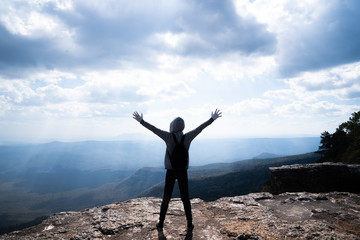 Obraz premium A person hands up standing on rocky mountain looking out at scenic natural view and beautiful blue sky