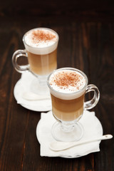Coffee in glass on the wooden background.  A glass with cappuccino and cinnamon. 