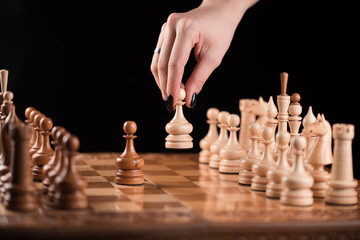 female hand making a chess move with a pawn on a chessboard on the black background.