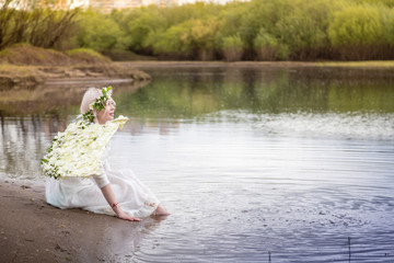 Fototapeta na wymiar Nice blonde girl with white flower wings near river
