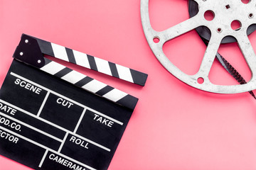 Filmings concept. Clapperboard and film stock on pink background top view copy space