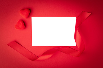 Blank paper note card with red ribbon bow on red background with hearts.