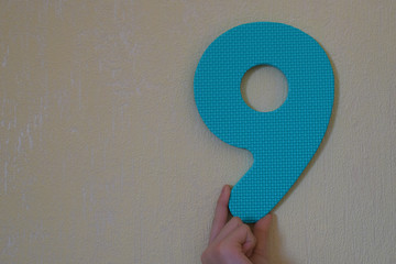 Hand holding blue number nine on mild yellow wall background with copy space for text. 9th...