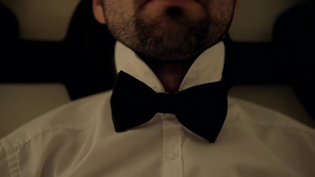Man Relaxing. A Man In White Shirt And Black Batterfly Sits On A Bed With Close Eyes.Man sitting on couch at home.Tie Butterfly close-up.Black bow tie close up.