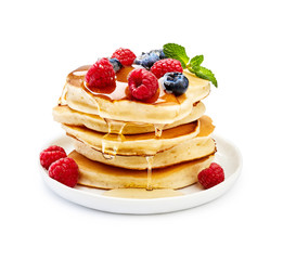 Delicious pancakes with berries, honey or maple syrup. Homemade pancakes and sweet syrup on white plate isolated.
