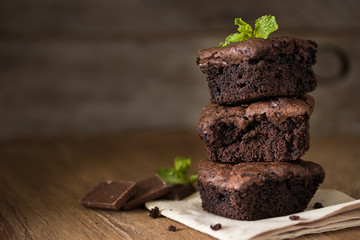 A stack of chocolate brownies on wooden background with mint leaf on top, homemade bakery and...