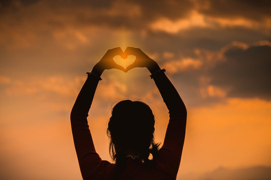 Women hands in the form of love and sunshine in the beautiful sky, the day of love, hands in the heart of love, love concept, heart-shaped hand gesture