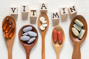 Variety of vitamin pills in wooden spoon on white background, supplemental and healthcare product,...