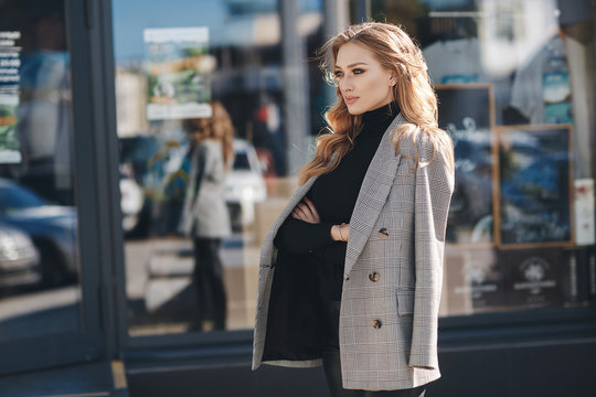 Portrait of beautiful woman with long curly blond hair outdoors in spring. Young woman with natural makeup in a gray jacket . A smart photo of a young beautiful woman in autumn clothes.
