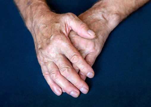 Hands of an elderly man folded together in close-up background
