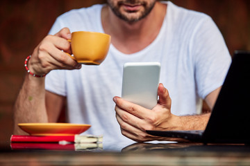 Man with smartphone, coffee / tea and laptop on a home porch.