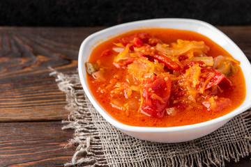 Homemade pickled salad of tomato, pepper, onion and carrot on dark wooden background.