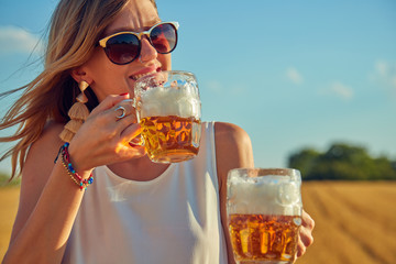 Happy girl holding beer glass in a big wheat-field.
