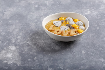 Smoothie bowl on gray background. Delicious mango smoothie topped with chia seeds, pieces of mango and dragon fruit. Word love made of cookie letters.  Healthy breakfast. Copy space.