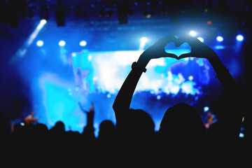 Girl with heart-shape symbol enjoying her favorite group on the concert.