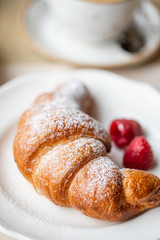 Coffee cappuccino with croissant on white plate in restaurant. Light morning Breakfast, fresh warm pastries and raspberries