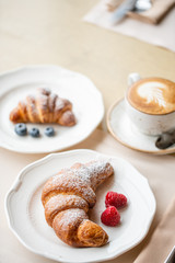 Coffee cappuccino with two croissant on white plate in restaurant. Light morning Breakfast, fresh warm pastries and raspberries