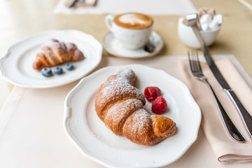 Coffee cappuccino with two croissant on white plate in restaurant. Light morning Breakfast, fresh warm pastries and raspberries