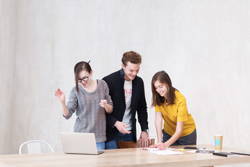 Creative team at work. Young positive people of the creative studio work together at large wooden table - looking at laptop and write down something