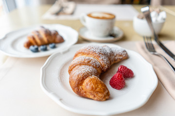 Coffee cappuccino with two croissant on white plate in restaurant. Light morning Breakfast, fresh warm pastries and raspberries