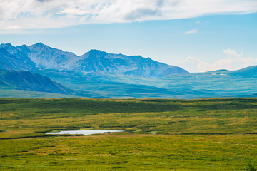 Huge mountain range at overcast weather. Creek and little lake before giant mountains under cloudy sky. Wonderful wild scenery. Dramatic highland landscape of majestic nature. Scenic mountainscape.