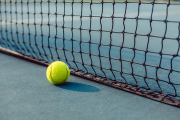 Close-up of a fluorescent yellow ball on blue acrylic surface in front of the net of a modern...