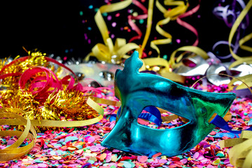 Close-up of blue carnival mask over confetti and multi-colored streamers