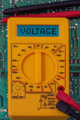 Digital multimeter multitester on a circuit board with the word voltage on the display