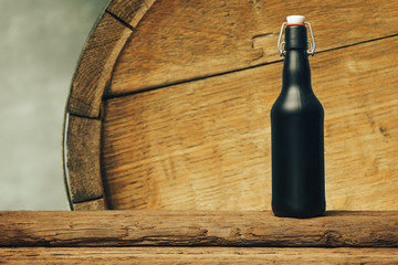 Black beer bottle on a old wooden table. Barrel background.