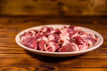 Ceramic plate with raw chicken hearts on wooden table