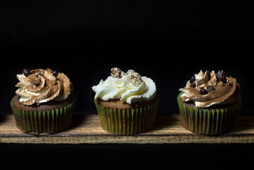 lighted cupcakes on a wooden board against a black background